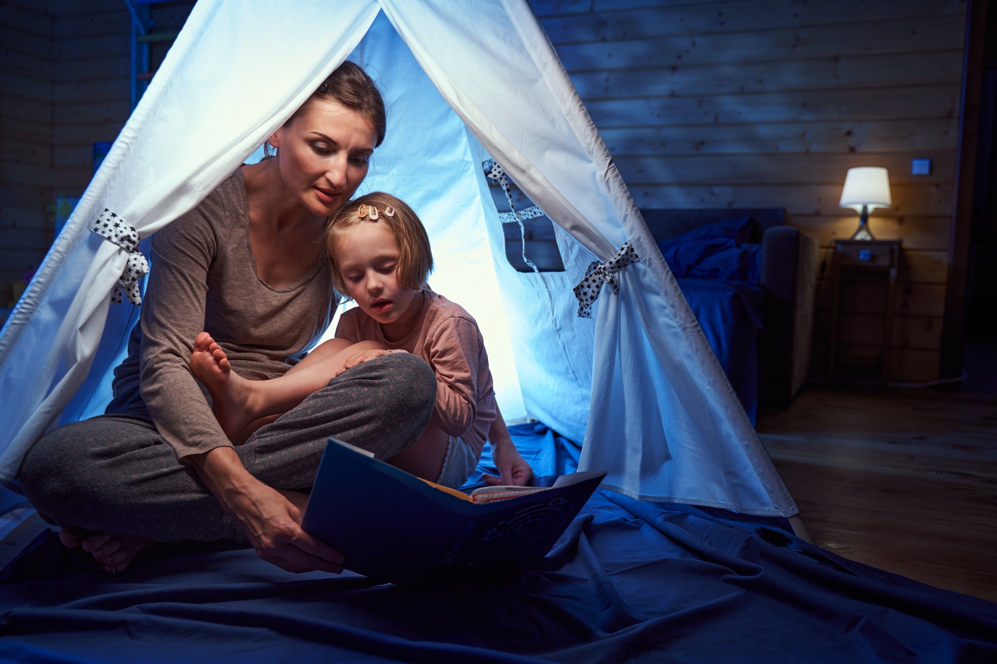 Adult and child in a tent at home reading book